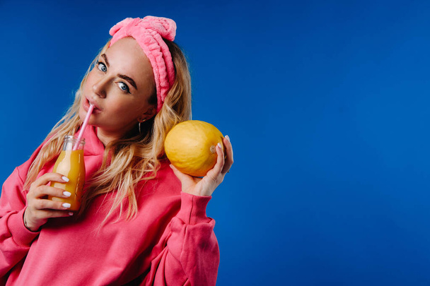 pregnant girl in pink clothes with a bottle of juice and a melon on a blue background. - 写真・画像