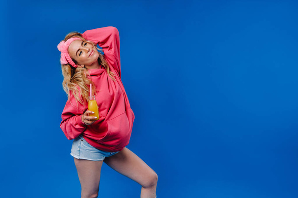 pregnant girl in pink clothes with a bottle of juice on a blue background. - Photo, image