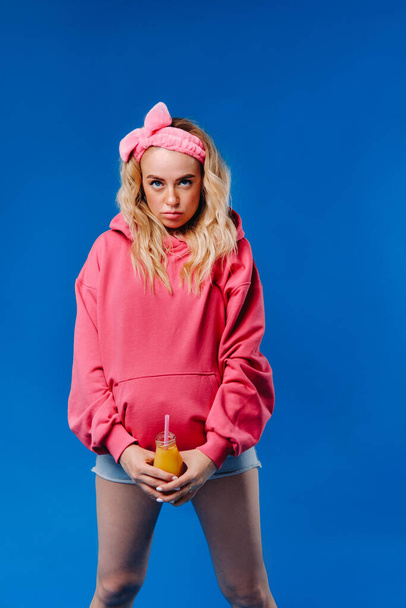 pregnant girl in pink clothes with a bottle of juice on a blue background. - Fotoğraf, Görsel