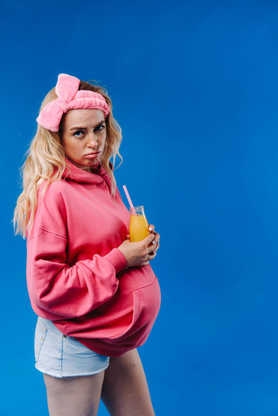 pregnant girl in pink clothes with a bottle of juice on a blue background. - Foto, immagini
