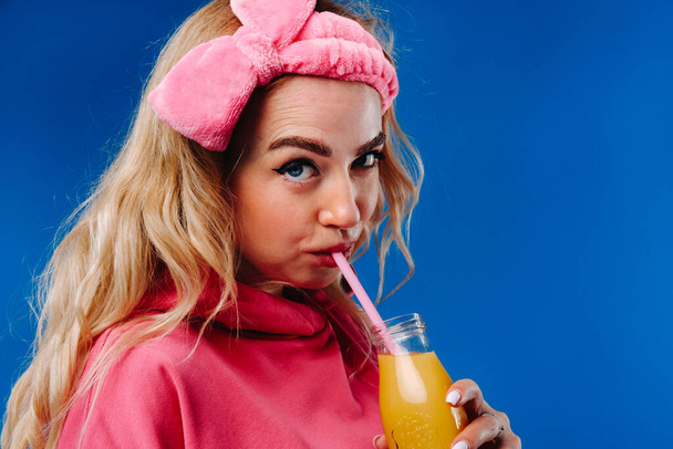 pregnant girl in pink clothes with a bottle of juice on a blue background. - Photo, image