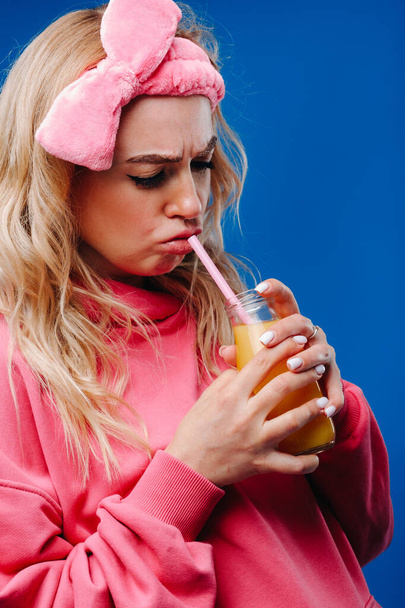 pregnant girl in pink clothes with a bottle of juice on a blue background. - Fotografie, Obrázek