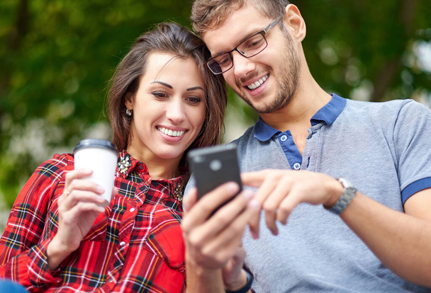 スマートフォンで幸せなカップル。一緒に屋外に立って一緒に携帯電話を見て幸せな若い愛情のカップル - 写真・画像