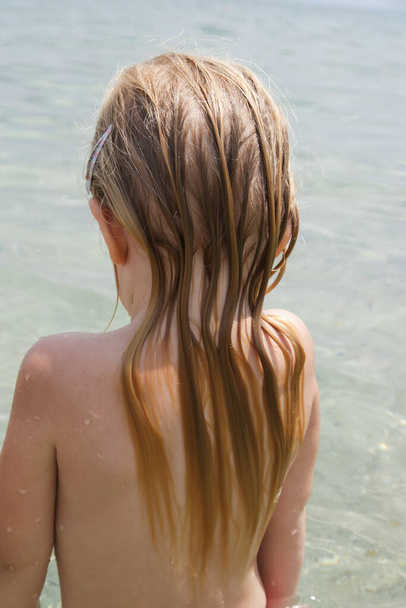 I capelli lunghi del bambino sulla spiaggia. Capelli bagnati primo piano immagine. Danni ai capelli dovuti all'acqua salata dell'oceano e al sole, concetto di cura dei capelli durante l'estate. - Foto, immagini