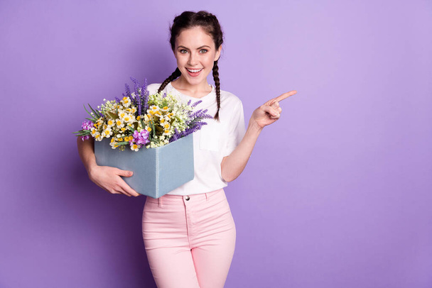 Photo of brunette braids haired lady wear casual clothes hold flowers box point finger empty space isolated on violet color background - Foto, afbeelding