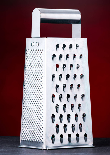Cheese grater with a dark red background. This photo was taken in a studio in London, Ontario   - Zdjęcie, obraz