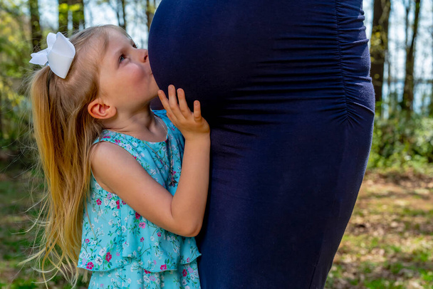 Uma bela mãe grávida posa com sua filhinha em um ambiente ao ar livre - Foto, Imagem