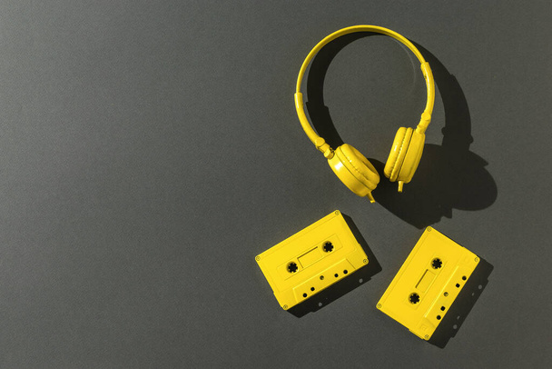 Keltaiset kuulokkeet ja kaksi nauhakasettia kirkkaassa valossa mustalla taustalla. Tilaa tekstille. Väritrendi. Vintage laitteet musiikin kuunteluun. Litteä. - Valokuva, kuva