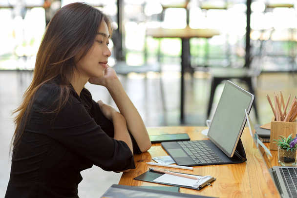 Aantrekkelijke vrouw die nadenkt over haar werk met slimme tablet met toetsenbord, briefpapier bij coffeeshop co-working - Foto, afbeelding