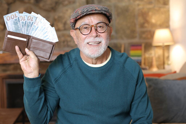 close-up portrait of handsome senior man holding wallet full of cash at home - 写真・画像