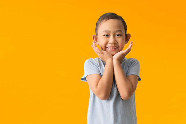 Happy asian child girl and smiles broadly expresses happiness feels joyful, isolated on yellow background  - Photo, image