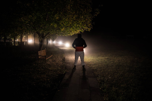 Silhouet van een persoon die met licht in het donkere bos staat. Horror halloween concept. vreemd silhouet in een donker spookachtig bos 's nachts - Foto, afbeelding