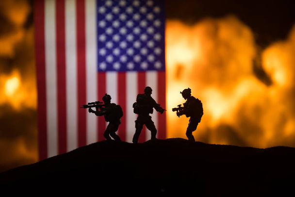 暗い背景に燃える上で米国の小さな旗。戦争の危機と国家間の政治的紛争の概念。アメリカの旗に対する武装した兵士のシルエット。選択的焦点 - 写真・画像