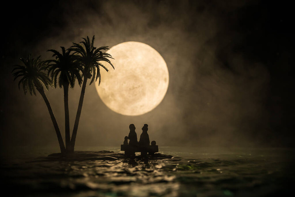 Romantisch nachtleven. Fantasie nacht landschap met kleine eiland met palmen en volle maan over zee. Creatieve tafeldecoratie. Silhouet van romantisch koppel op onbewoond eiland. Selectieve focus. - Foto, afbeelding