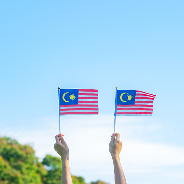 χέρι κρατώντας τη σημαία της Μαλαισίας σε μπλε φόντο του ουρανού. Σεπτέμβριος Μαλαισία εθνική ημέρα και Αύγουστος Ημέρα Ανεξαρτησίας - Φωτογραφία, εικόνα
