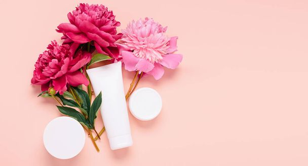 Produits cosmétiques gel crème shampooing baume dans diverses bouteilles sur un fond rose avec des pivoines de fleurs fraîches - Photo, image