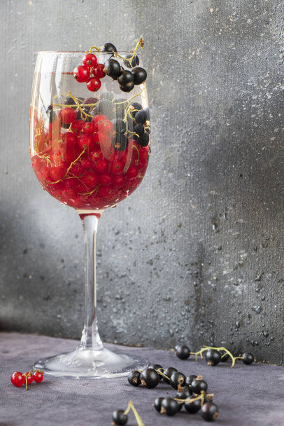 Fresh red and black currants in a wine glass on a gray background - Foto, imagen