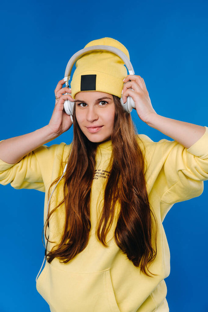A pregnant girl in a yellow jacket and headphones stands on a blue background. - Foto, immagini