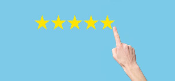 Człowiek trzyma smartfon w rękach i daje pozytywną ocenę, ikona pięć symbol gwiazdy, aby zwiększyć rating koncepcji firmy na niebieskim tle.Customer service experience and business satisfaction survey - Zdjęcie, obraz