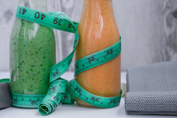 Mevsimlik Matcha yeşil vejetaryen smoothie ve balkabağı havuçlu smoothie ölçüm bandı ve lastik dirençli detoks kahvaltısı. Stretch fitness bandı. Temiz yemek, kilo kaybı, sağlıklı beslenme konsepti. Evde sağlıklı kalmak. - Fotoğraf, Görsel