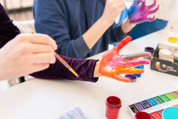 Women paint their hands with colored paints in the classroom. - 写真・画像