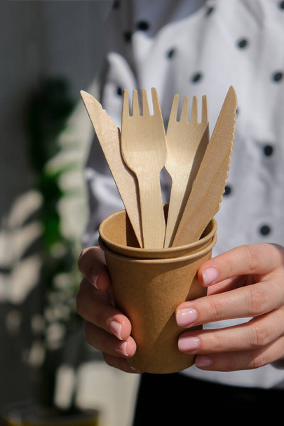 Female hands holding Wooden forks and paper cups with plates. Eco friendly disposable tableware. Used in fast food, restaurants, takeaways, picnics. No plastic Zero waste - Фото, изображение