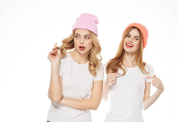 zwei Frauen in weißen T-Shirts Hüte auf dem Kopf Mode Kommunikation heller Hintergrund - Foto, Bild