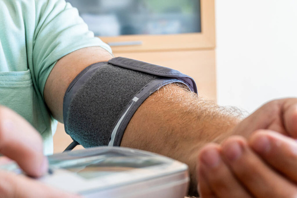 Arm van een man die de bloeddruk controleert met een bloeddrukmeter.  - Foto, afbeelding