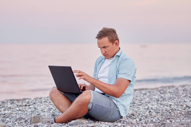 Мужская брюнетка с ноутбуком на пляже. Фрилансер, работающий в режиме реального времени, веб-бинар, обучающийся концепции, общающийся с друзьями. Новая нормальная концепция - Фото, изображение