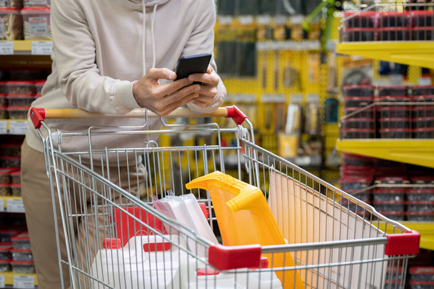 Nuori mies vieritys älypuhelin yli ostoskorin - Valokuva, kuva