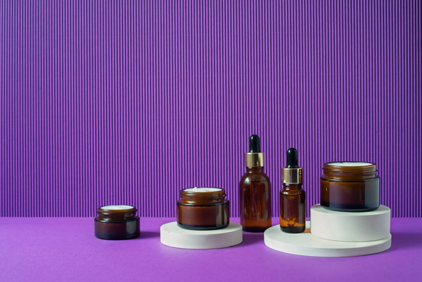 Bottiglie e barattoli di vetro ambrato dalle forme geometriche di tendenza su sfondo viola. Bianco - Foto, immagini