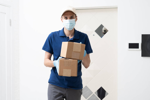 Auslieferer mit Schutzmaske und Handschuhen hält Box mit Lebensmitteln vor der Tür - Foto, Bild
