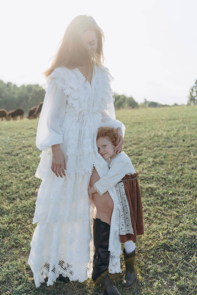 Красивая женщина в белом кружевном платье проводит время со своей маленькой рыжей дочерью на поле - Фото, изображение