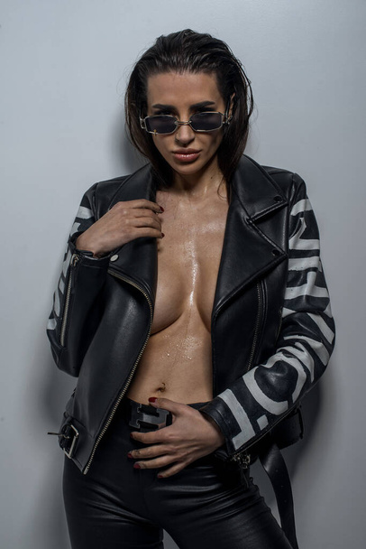 fashionable  young  woman  in sunglasses and leather jacket posing in studio  - Fotografie, Obrázek