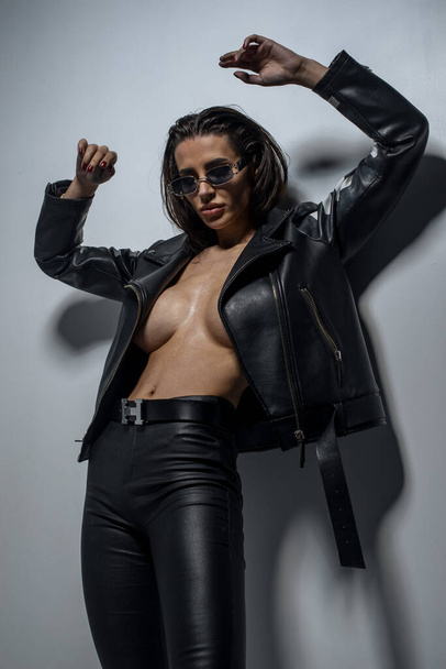 fashionable  young  woman  in sunglasses and leather jacket posing in studio  - Zdjęcie, obraz