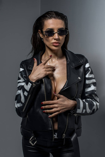 fashionable  young  woman  in sunglasses and leather jacket posing in studio  - Foto, Imagem
