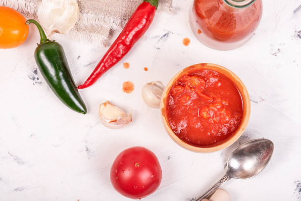 Інгредієнти для приготування мексиканського гарячого соусу - помідори, чилі і халапенос, часник, подрібнені помідори в чашці і готовий соус у пляшці на світлому тлі, вид зверху, плоский
 - Фото, зображення