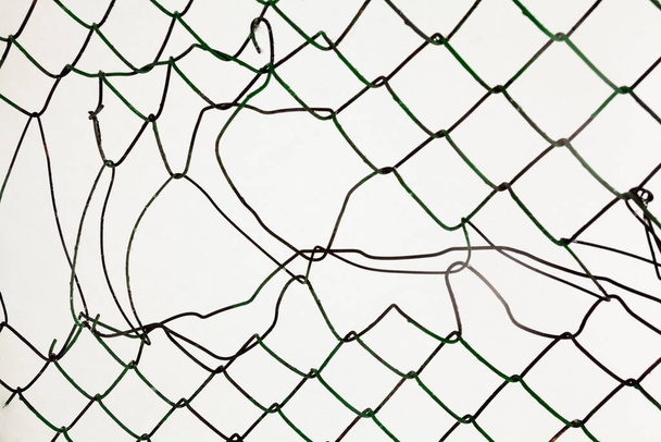 Broken metal mesh fence against the gray sky. - Photo, Image
