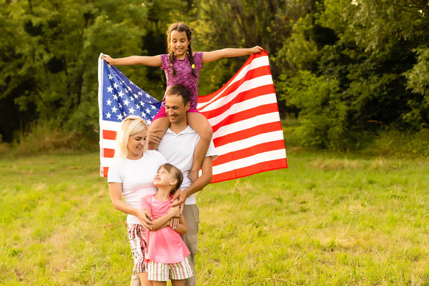 Gelukkige familie met de Amerikaanse vlag in een tarweveld bij zonsondergang. Onafhankelijkheidsdag, 4 juli. - Foto, afbeelding