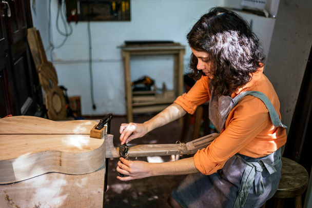 vrouw luthier maken van gitaren in haar muzikale instrument workshop - Foto, afbeelding