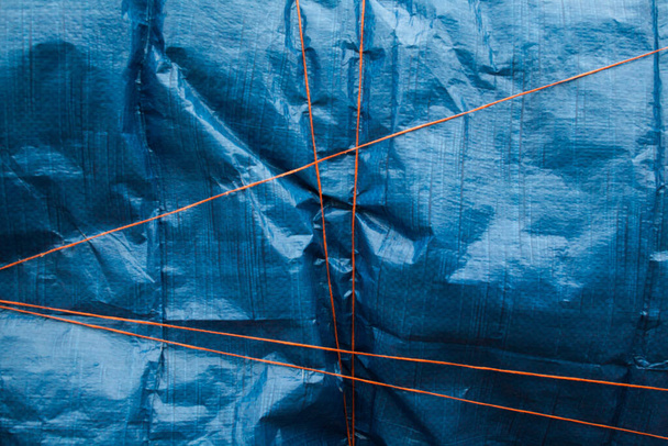 Blue crumpled synthetic fabric tied up with orange thread. Abstract background. - Photo, Image