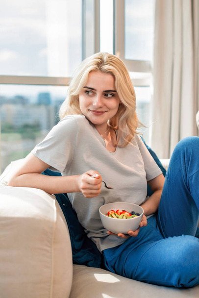 Junge blonde Frau auf einem Sofa mit gesundem Haferbrei - Foto, Bild