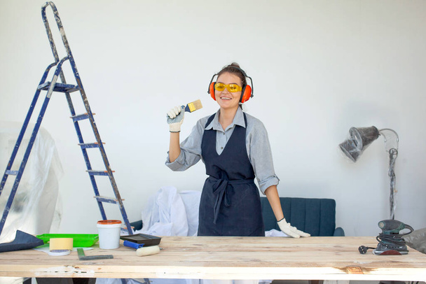 眼鏡手袋とヘッドフォンの若い暗い髪の女性は、建設ワークショップで働く準備ができて笑顔 - 写真・画像