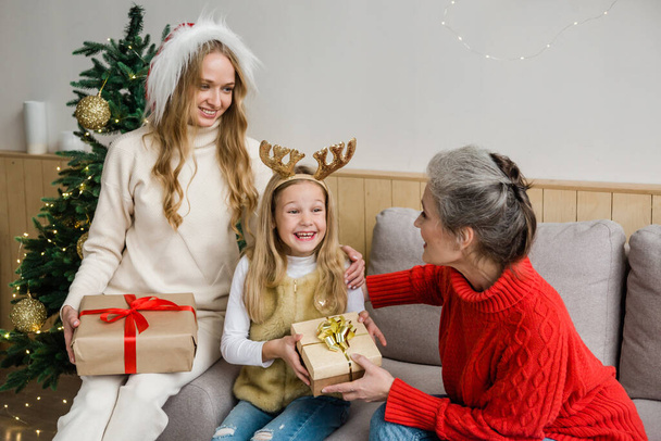 Rodinný koncept samoživitelky. Babička, máma a veselá holka si vyměňují dárky. Rodiče a dcery se baví ve vánočním zdobeném pokoji. Rodinná dovolená - Fotografie, Obrázek