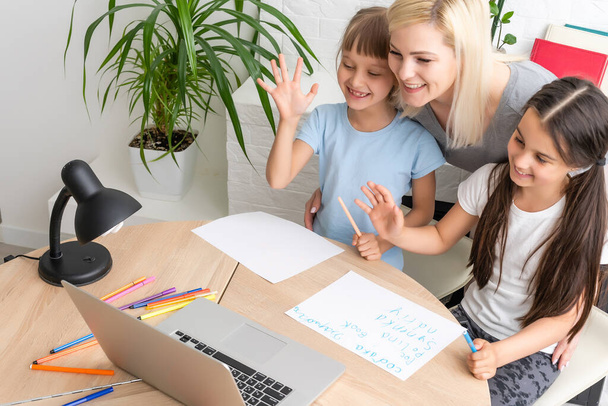 Woman tutor or foster parent mum helping cute caucasian school child girl doing homework sitting at table. Diverse nanny and kid learning writing in notebook studying at home - Foto, Imagem