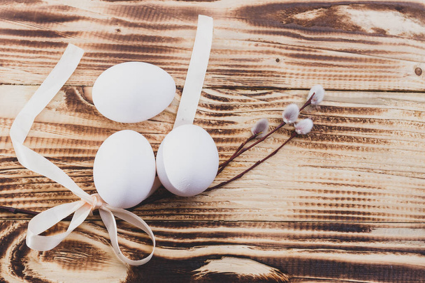 Easter white eggs are tied with a ribbon with a willow for the Easter holiday on a brown wooden natural table. - Photo, image