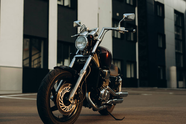 A motorcycle in a parking lot in the warm light of a sunset. Stylish custom chopper motobike with chrome details. Freedom, motorcycle travel. Soft selective focus. - Foto, Imagen