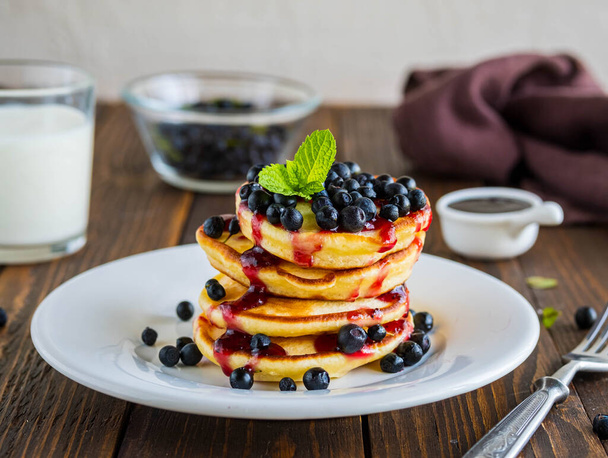 Pancakes with corn flour, blueberries and berry jam on a white plate on a brown wooden background. Pancake recipes. - Photo, Image