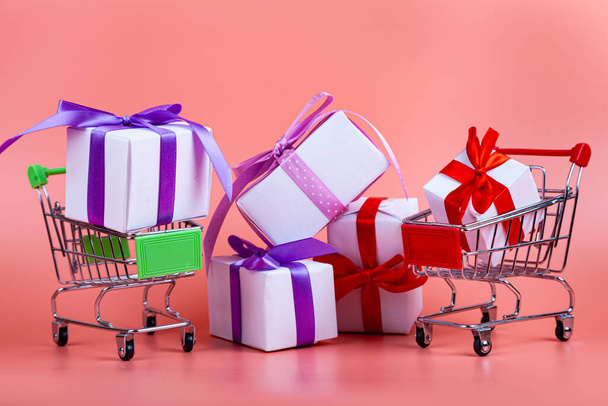 Shopping carts and gifts on a pink background. Concept: buying gifts. - Foto, Bild