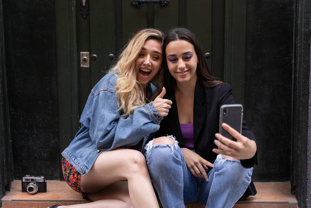 Dos chicas sonriendo tomando una selfie mientras están sentadas en la calle - Foto, Imagen